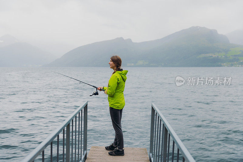 身穿绿夹克的女子在挪威峡湾钓鱼