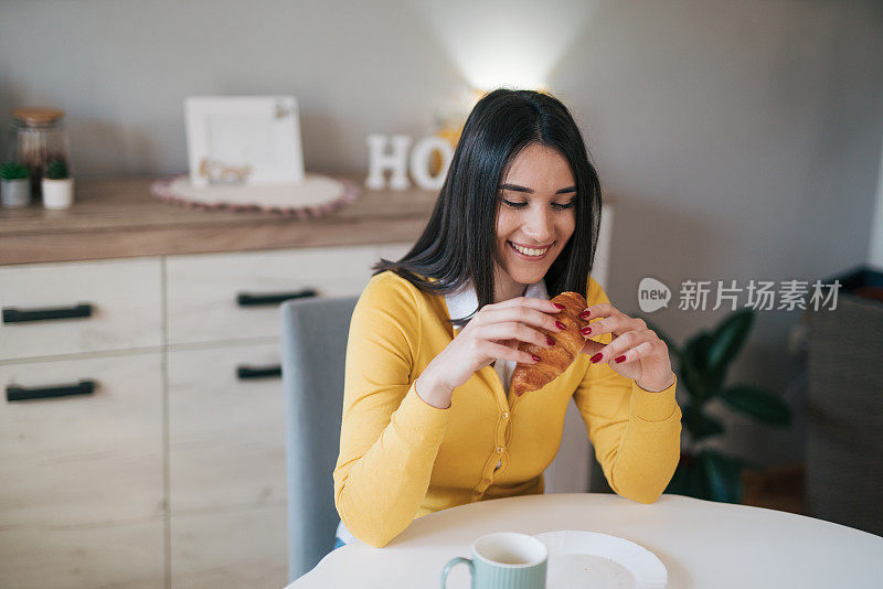 年轻女子在厨房吃牛角面包