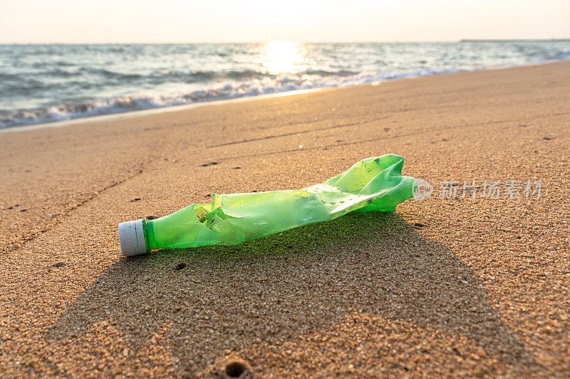 一个由PET制成的绿色软饮料瓶留在海滩上，被环境和海水降解，导致微塑料和环境问题