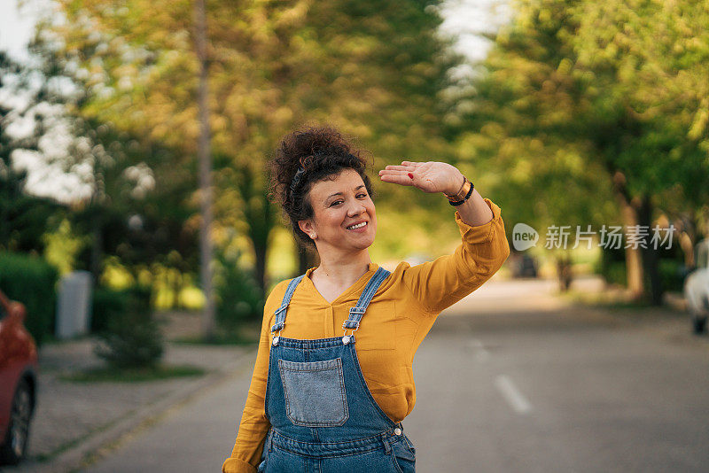 一个微笑的女人站在街上向某人挥手。