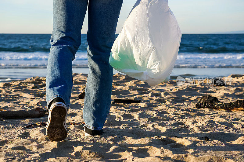 拿着垃圾袋的人在海滩上清理