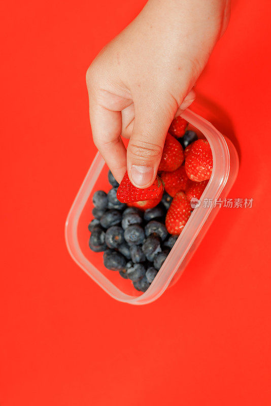 手拿草莓，包括蓝莓在塑料盒的背景