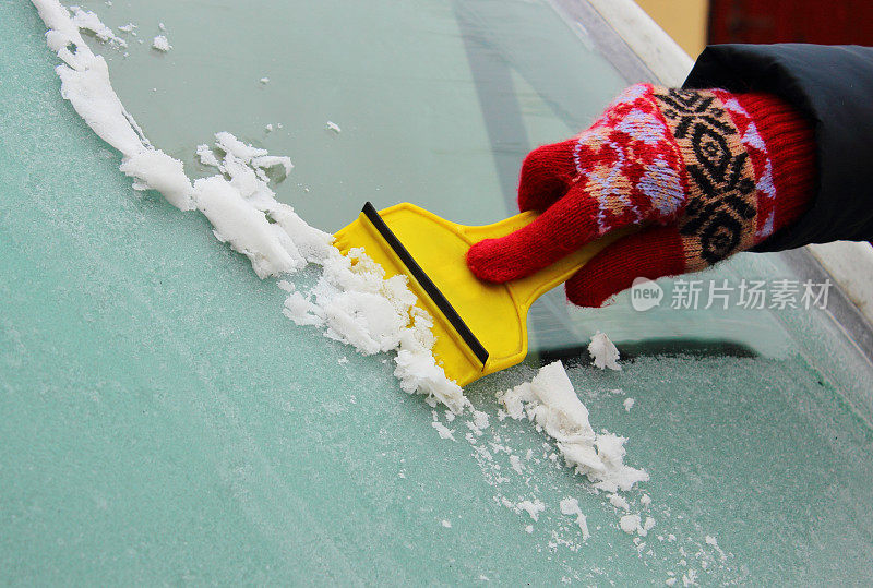 女人的手从汽车挡风玻璃上刮冰