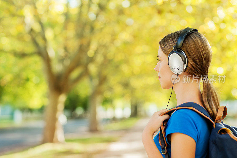 背着书包戴着耳机在校园里听音乐的女孩