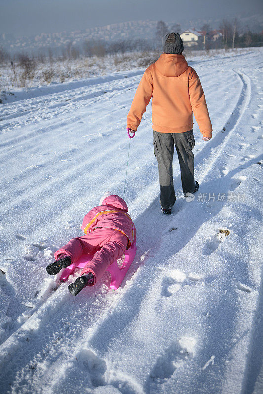 父亲拉着女儿在雪橇上