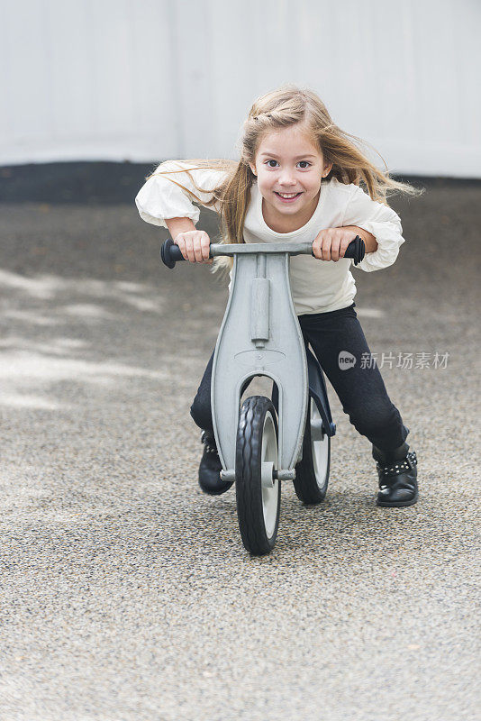 小女孩在操场上骑着玩具踏板车