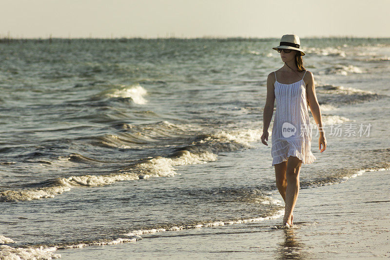 美丽的女人穿着白色漫步在荒芜的海滩