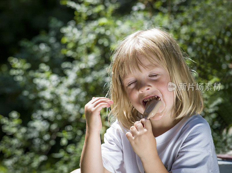夏日阳光下吃冰淇淋的金发小女孩。