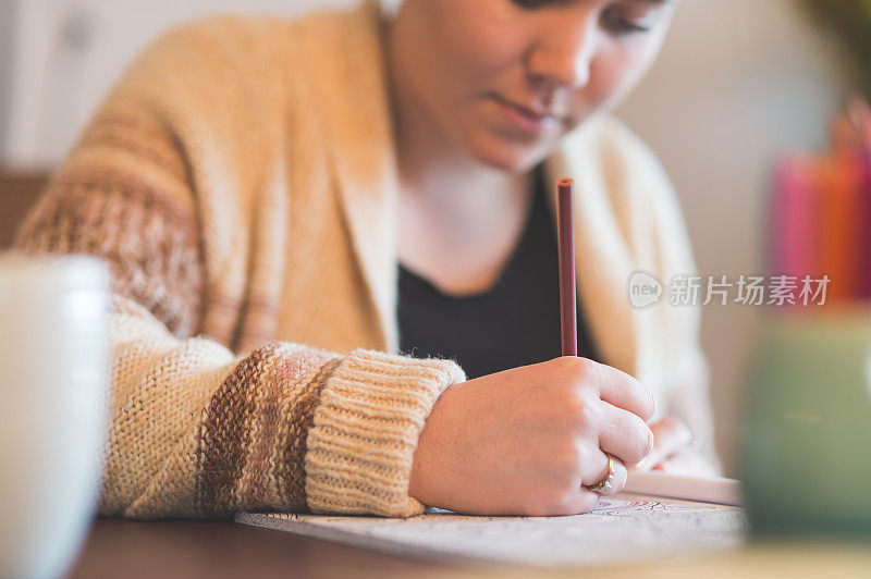 年轻迷人的女人在成人着色书在桌子上画画