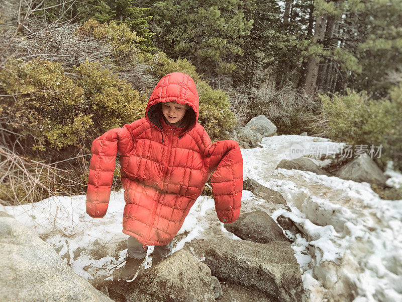 小男孩穿着爸爸的夹克走在雪山里