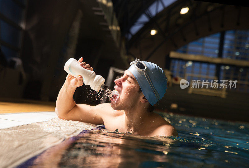 男性游泳者在泳池边喝着一个水瓶里的水