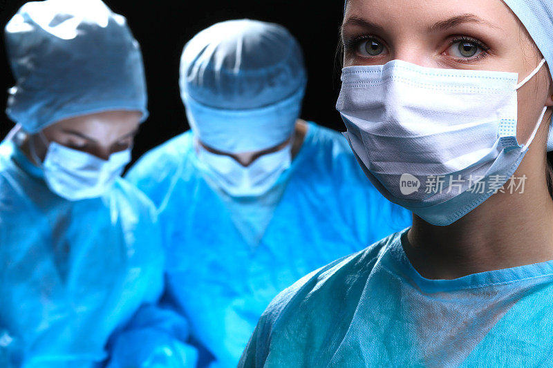 三个外科医生在外科手术室里做手术抢救病人并观察生命监视器。抢救队医戴着防护口罩。手术和急诊概念