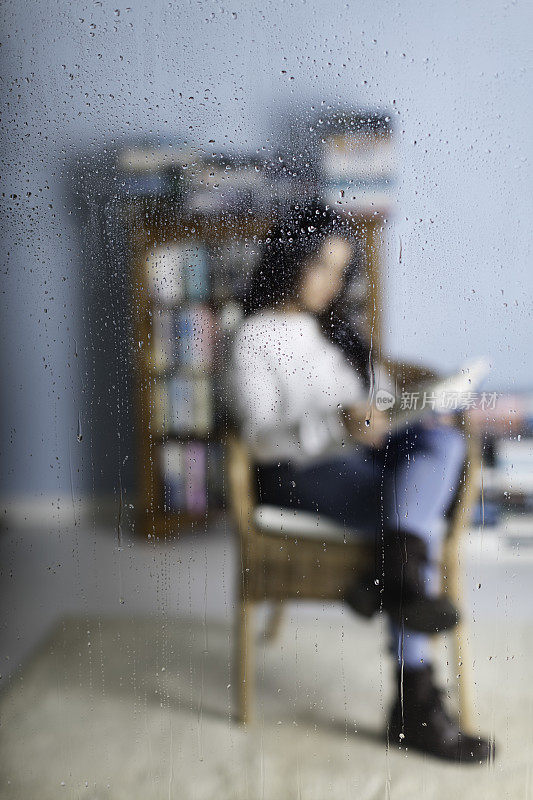 女孩躲在一扇被雨水打湿的窗户后面