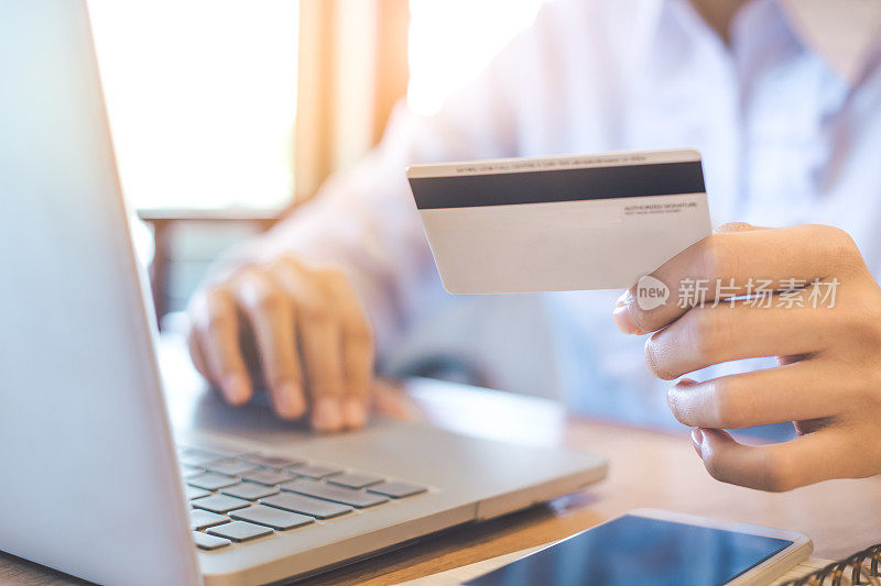 一位女士手里拿着一张信用卡，用笔记本电脑在网上购物。