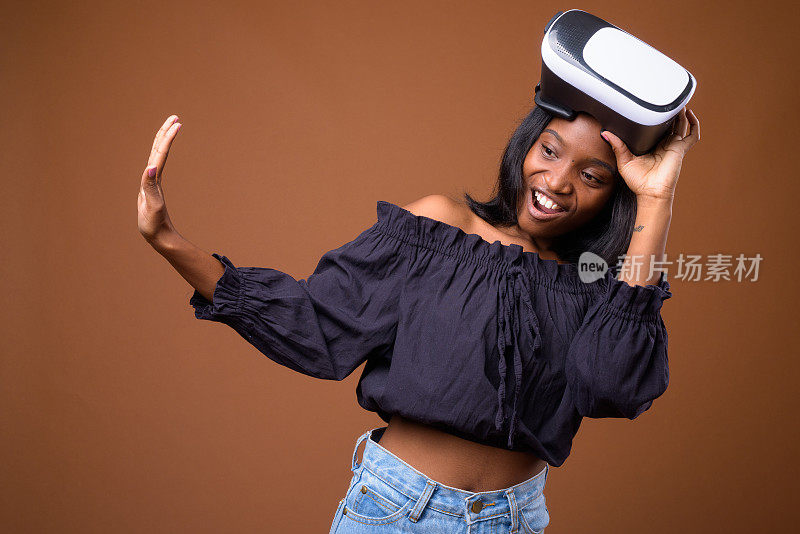工作室拍摄的年轻美丽的非洲祖鲁妇女使用虚拟现实头盔的彩色背景