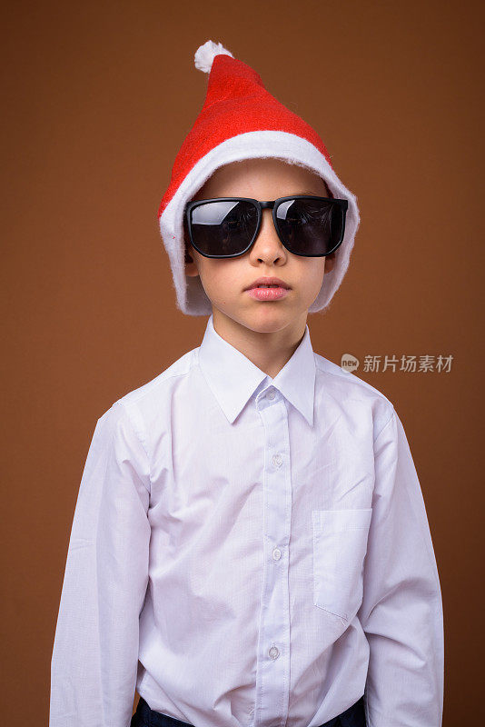 在彩色背景下，小男孩扮成商人戴着圣诞帽准备迎接圣诞节