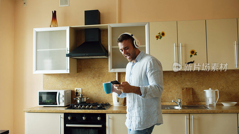 英俊的年轻有趣的男人戴着耳机在厨房跳舞和唱歌，在家里的早上和有乐趣的假期