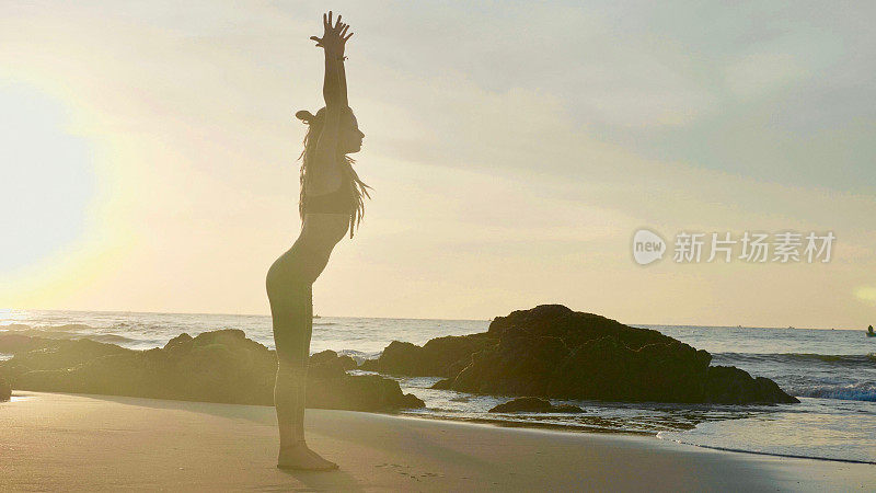 日落时练习剪影瑜伽。一个年轻女人在海滩上做瑜伽运动