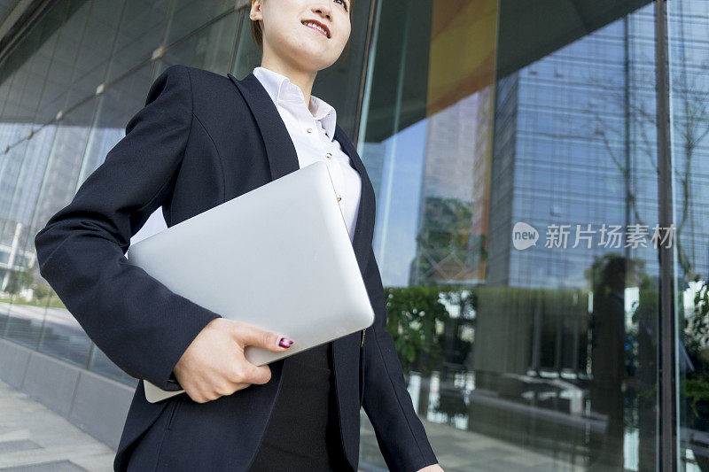 一名女商人拿着笔记本电脑在城市中行走