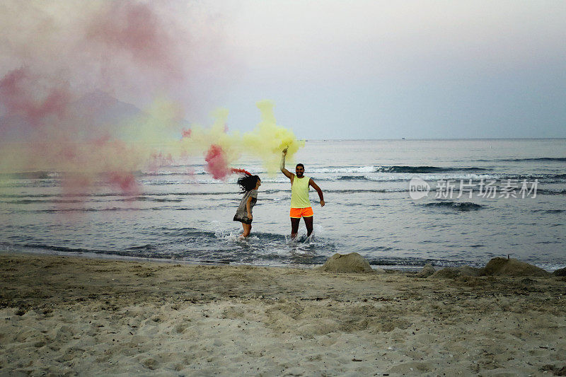 浪漫的情侣与黄色和红色的烟雾弹在海滩上