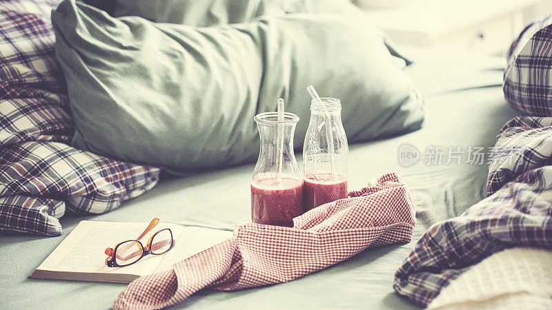 皱巴巴的床上用品与新鲜的粉红色水果冰沙和书一个轻松的一天
