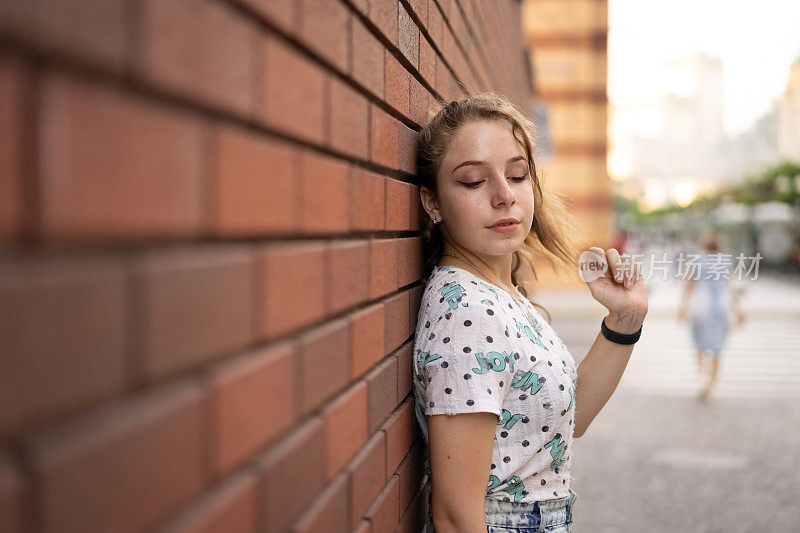 一个十几岁的女孩站在一堵砖墙旁边向下看