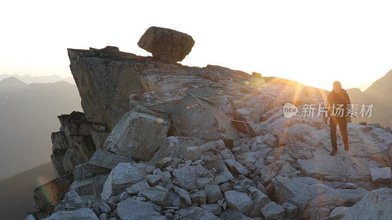 登山者在日出时徒步爬上岩石的顶峰