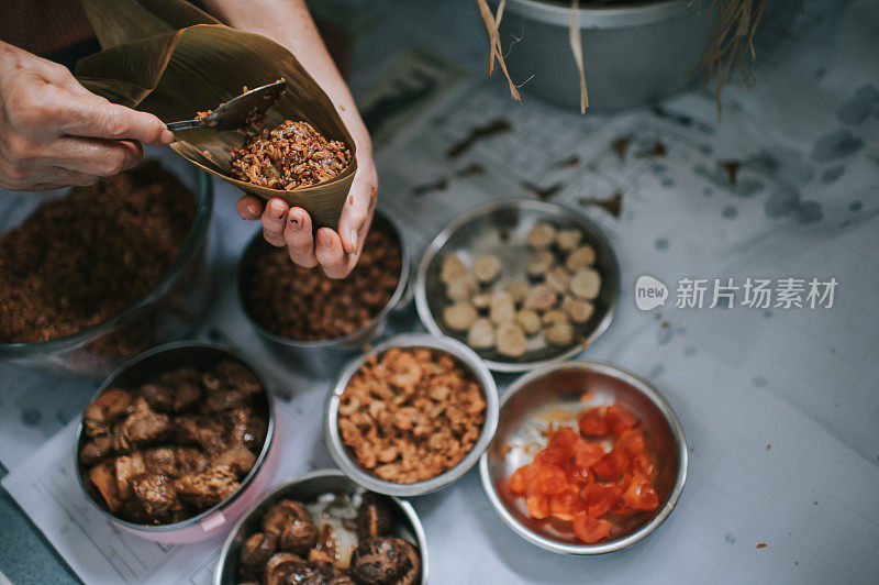 一位年长的亚洲华人妇女在她的厨房里准备粽子，把配料包好，为端午节做准备