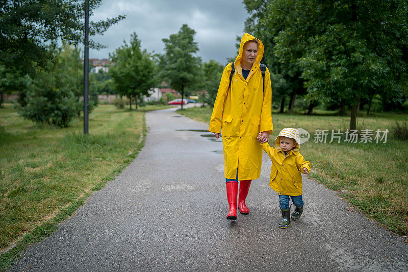 母亲和一个孩子。母亲和儿子穿着雨衣，手牵着手在公园里