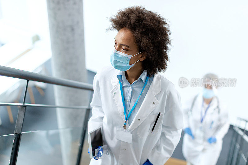 戴着面罩的非裔美国女医生走上楼梯，看向别处。