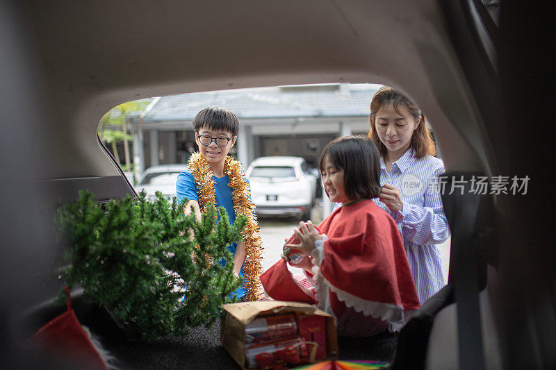 亚洲华人家庭从车上取下圣诞装饰和圣诞树。他们正在准备圣诞节庆祝活动。