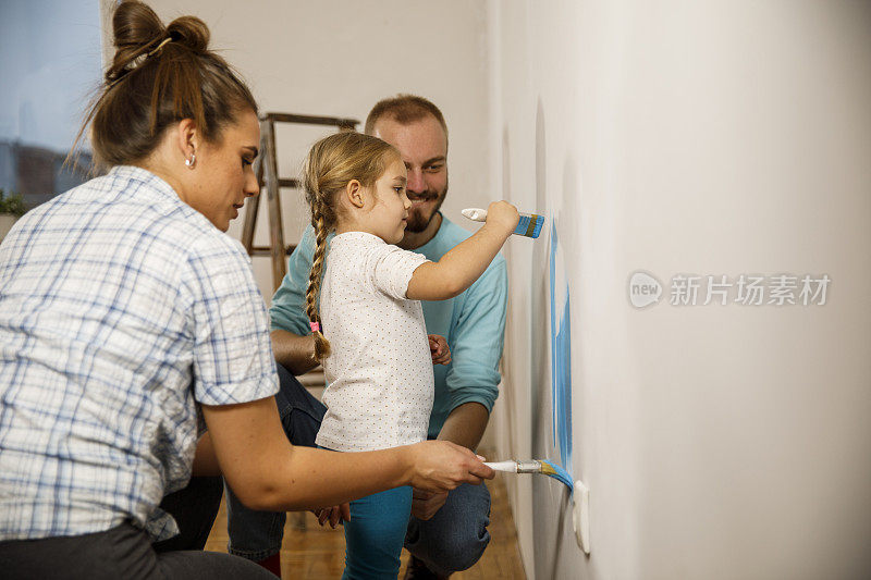 可爱的小女孩帮她的父母把墙漆成蓝色的侧视图