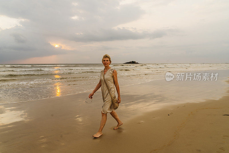 成熟迷人的50岁欧洲女人，一名游客，走在热带海滩上的日落。