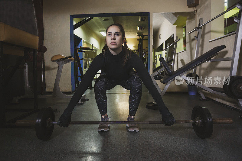 美丽的女运动员在健身房用杠铃和重量练习硬举