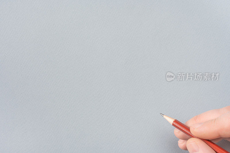 用铅笔在灰色的纸上写东西。特写的人的手与铅笔。在灰色纸模板上用铅笔手绘。本空间