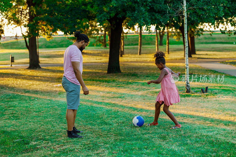 一个快乐的非裔美国人家庭正在草地上玩足球。
