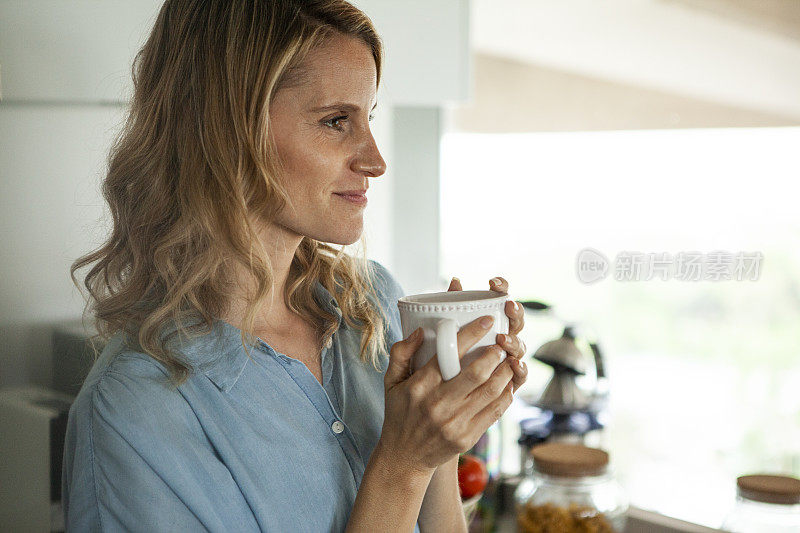 微笑的中年妇女拿着一杯茶，而站在厨房白天