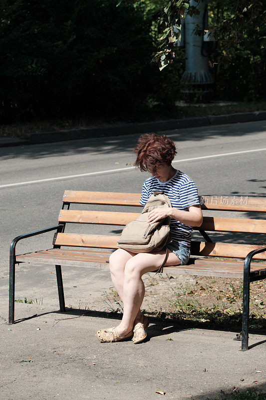 一个女人坐在长凳上，在她的背包里找东西