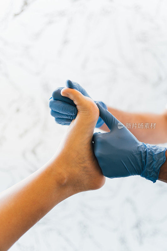 近距离的手足病医生的手与医用手套探索的脚病人在足病诊所。