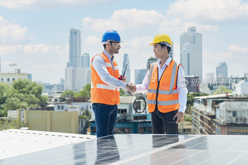 屋顶上的太阳能电池板技术员。工程师和年轻的技术人员在风力太阳能电站周围握手。