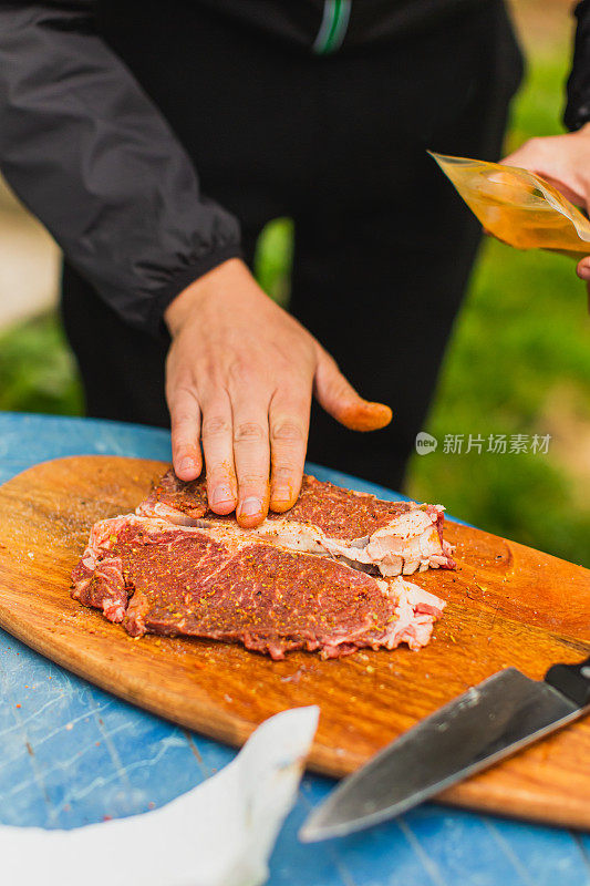 新鲜牛排。满足户外经验。晚餐在后院。木板上红肉。准备食物的过程。小牛肉。美味的小吃。户外用餐。盐和调味食品