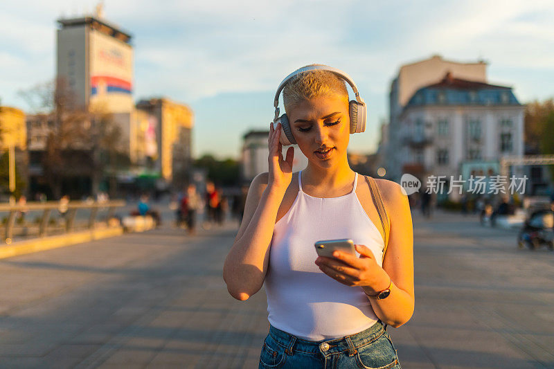 美丽的年轻女子，金色短发，一边听音乐，一边穿过城市