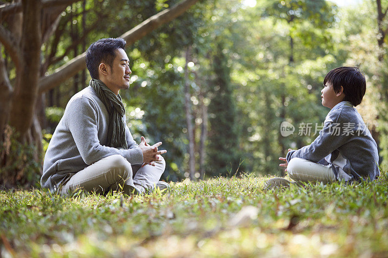 年轻的亚洲父亲与儿子在户外愉快地交谈