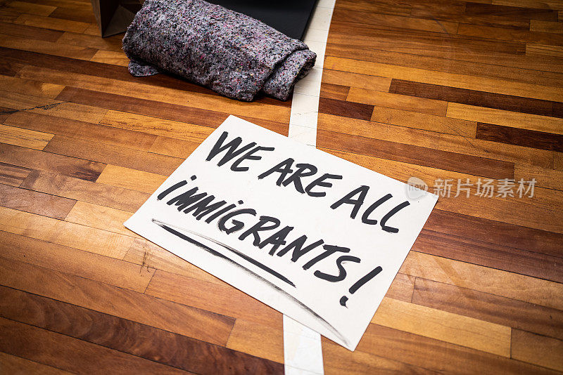 地上的牌子上写着“我们都是移民!”