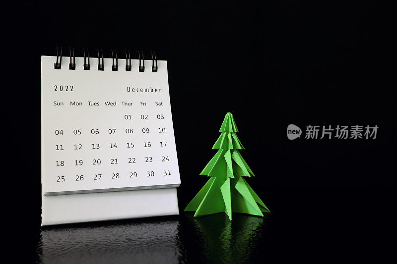 你好，2022年12月，圣诞概念。书桌日历与圣诞树上的黑色背景。