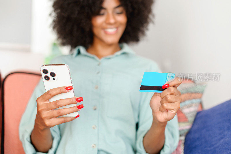 在线购物。选择性地关注快乐黑人女性手中的智能手机和信用卡，女学生在家网上购物