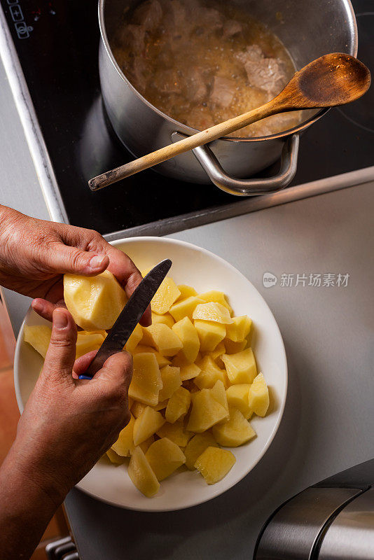 在家里的厨房里，女人用手把土豆切成小块，加入炖肉的锅里。