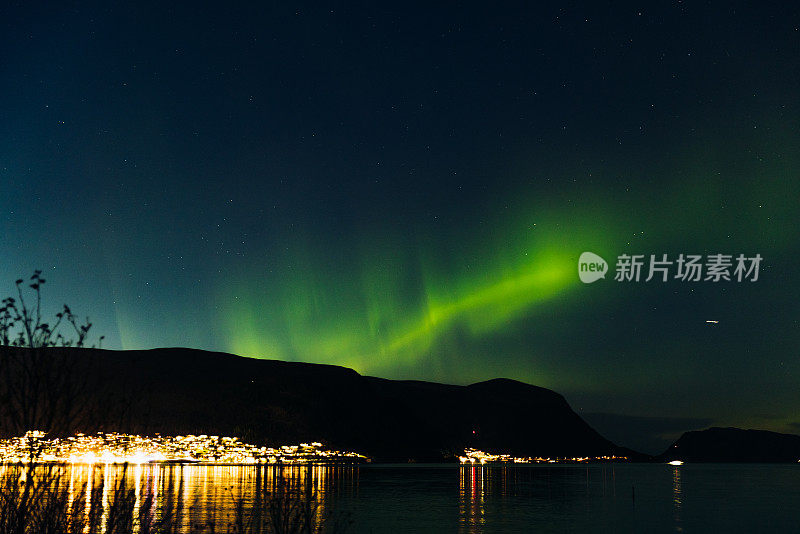 风景秀丽的北极光在峡湾和发光的城镇在挪威