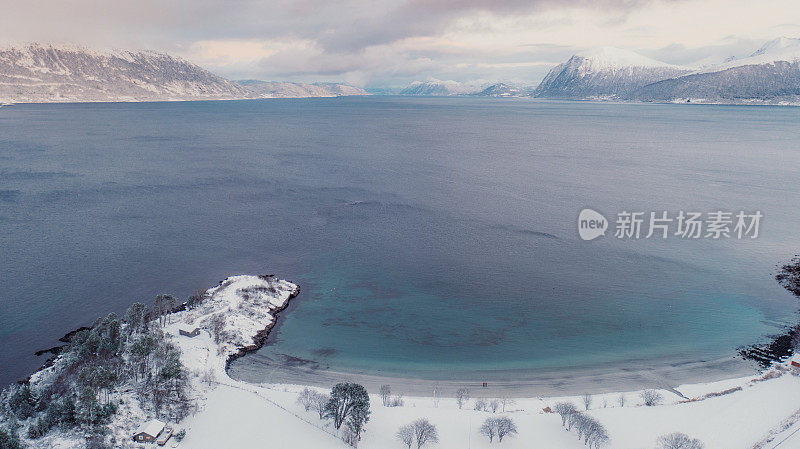 航拍图像的女人和男人走在风景秀丽的turqouse海滩在雪与山景在挪威