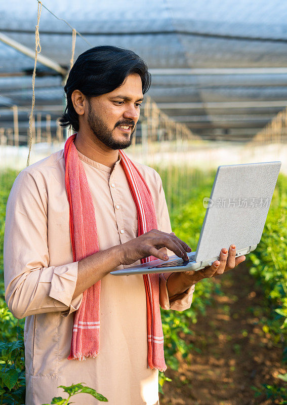 快乐的年轻农民在温室的笔记本电脑上忙碌的垂直镜头-现代农业的概念，技术和发展或增长。